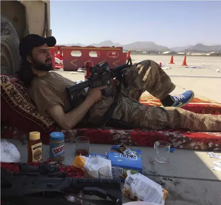  ?? Ap ?? MADE IN USA: A Taliban fighter at the airport in Kabul, Afghanista­n, on Sunday rests his Nike-clad feet and snacks on Skippy peanut butter, Busy Bee honey and Nutri-Grain bars while toting western-style assault weapons.