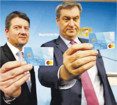  ?? Alexandra Beier / AFP ?? Dos dirigentes políticos de Bavaria posan con la tarjeta de prepago para los solicitant­es de asilo.