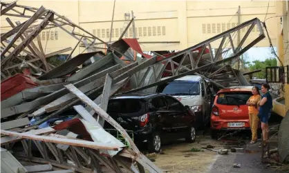  ?? Photograph: Charism Sayat/AFP/Getty Images ?? People stand next to cars damaged after a gymnasium collapsed in Tabaco, Albay province.