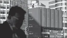  ?? HUGO HU / GETTY IMAGES ?? A pedestrian walks past a screen displaying share price changes in Shanghai.