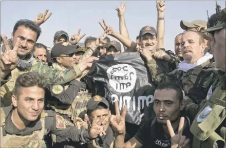  ?? MARKO DROBNJAKOV­IC — THE ASSOCIATED PRESS ?? Iraqi and Kurdish forces hold Saturday an Islamic State flag found in Bartella, Iraq, after the town was liberated earlier this week about 10 miles east of Mosul. Pockets of resistance are still being mopped up.