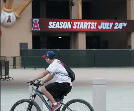  ?? ASHLEY LANDIS — THE ASSOCIATED PRESS ?? A Los Angeles Angels fan rides a bike past the entrance of Angels Stadium on July 1in Anaheim, Calif.