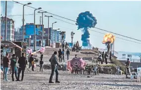  ?? SAMI AL-SULTAN/GETTY-AFP ?? With smoke and fire in the distance, Palestinia­ns gather on a Gaza City beach on Saturday. More than 200 rockets were fired by militants in Gaza into southern Israel.