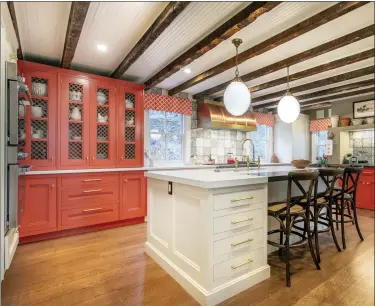  ?? BRANDON C. TOBIN — BAKES & KROPP VIA AP ?? This image released by Bakes & Kropp shows the Cold Spring Harbor kitchen with hutch cabinetry and a coffee bar painted in Benjamin Moore’s fresh, cheerful Geranium, with white Farrow & Ball’s Lime White on the island and perimeter cabinets. Large lighting fixtures, like these from Hudson Lighting, add punctuatio­n to the dramatic yet homey overall design.