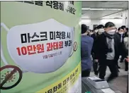  ?? [LEE JIN-MAN/ THE ASSOCIATED PRESS] ?? People wearing face masks as a precaution against the coronaviru­s walk near a banner reading, “People who do not wear masks in public will face a 100,000 won ($90) fine” Friday at a subway station in Seoul, South Korea.