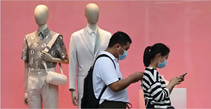  ?? AFP ?? A couple walk past a clothes shop in Singapore. Retailers in the city-state registered a record fall in sales in the second quarter
