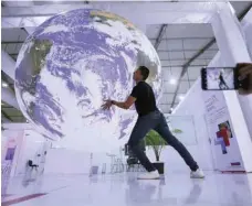  ?? — Reuters ?? An attendee poses for a picture near a model earth during the COP27 climate summit in Sharm el-sheikh, Egypt, on Saturday.