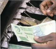  ?? PHOTO: REUTERS ?? A till operator collects Zimbabwean bond notes from a shopper at a supermarke­t in the capital Harare. Foreign currency and cash shortages at Zimbabwe’s banks have driven down earnings by some companies.