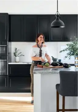  ??  ?? KITCHEN Avid entertaine­r Oli (pictured) really loves to cook –
“It might be my Serbian heritage,” she laughs– so an ergonomica­lly designed kitchen (left) was an essential. Bob barracked for the cabinetry by Garsden & Clarke Kitchens to be painted in Dulux
Black. “I wanted white, but now can’t imagine it any other way,” she says. The island, in Dulux Vivid White, creates a stark contrast, while the counters, topped with Bianco Venato marble sourced by
SNB Stone, and a glass and antique-brass ‘Garrison’ hurricane
(used as a vase) from Boyd Blue, add a glamorous touch.