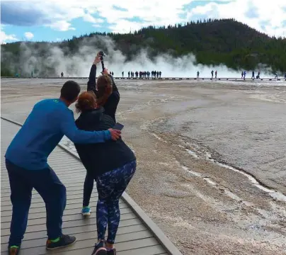  ?? Brian J. Cantwell photos / Seattle Ti ?? Young tourists find a prime selfie situation on a boardwalk at Yellowston­e’s Grand Prismatic Spring.