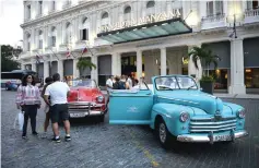  ??  ?? Tourists stand next to an old American car in front of the Gran Manzana Hotel in Havana.