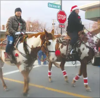  ?? Westside Eagle Observer/ SUSAN HOLLAND ?? Two horseback riders on colorful paint ponies smile at the crowd as they make their way down Gravette Main Street. These two riders were part of a small group of horsemen who entered the annual Christmas parade and dressed their horses with wreaths around their necks and big red bows on their tails.