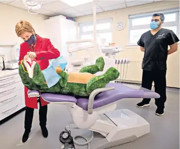  ??  ?? First Minister Nicola Sturgeon practices checking teeth on a model dinosaur, during a visit to Thornlieba­nk Dental Care centre, Glasgow