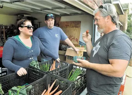  ?? Jerry Baker photos ?? Brandi McRill, from left, with her husband Jack, visits with Michael Marchand as he taste-tests a strawberry which was part of the week’s produce “share,” which cost each member $30.