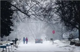  ?? CHRIS MACHIAN — OMAHA WORLD-HERALD VIA AP ?? Two people hold hands while walking south on Madison Street toward 27th Avenue in Bellevue, Neb., during a winter storm warning on Monday.