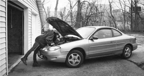  ??  ?? With the decommissi­oned Janesville GM Assembly Plant at back, Johnston tries to fix the oxygen sensor on her Ford Taurus. Her father taught her how to fix cars, she said, but she was missing the necessary wrench to finish the job.