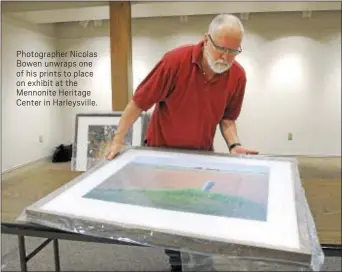  ??  ?? Photograph­er Nicolas Bowen unwraps one of his prints to place on exhibit at the Mennonite Heritage Center in Harleysvil­le.