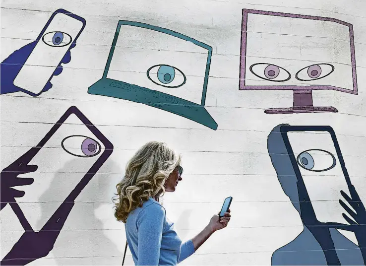  ?? ANDREW BRET WALLIS / GETTY ?? Una dona caminant mentre mira el mòbil amb un mural que representa l’espionatge amb dispositiu­s de pantalla
