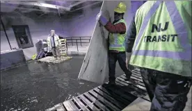  ?? JULIO CORTEZ / ASSOCIATED PRESS ?? On Friday, New Jersey transit workers lay boards for commuters to walk on in a flooded hall adjacent to the site of the deadly train crash in Hoboken.