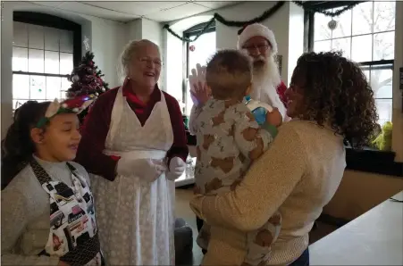  ?? MICHELLE LYNCH — MEDIANEWS GROUP ?? Mr. and Mrs. Santa Claus, played by Ben and Amy Schiavone of Exeter Township, greet a young resident of Opportunit­y House, held by volunteer Jana Bryant of Reading. Volunteer Carmen Jordan, 10, is at left.