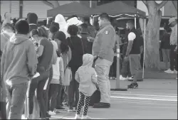  ?? EDUARDO CONTRERAS/SAN DIEGO UNION-TRIBUNE ?? Members of the Mexican government organizati­on called Grupo Beta (man with Mexican flag on shoulder) oversee and administer the process of migrants seeking asylum in the U.S. on April 18 during a morning gathering at the El Chaparral plaza in Tijuana, Mexico.