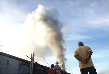  ?? AP FOTO ?? MARAWI BURNS.
Residents look at a burning structure during early morning airstrikes by government forces in the continuing fight for Marawi City by Muslim militants. Fighting enters its second month.