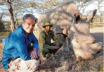  ?? Foto: Markus Strobel, ZDF, dpa ?? Schauspiel­er Hannes Jaenicke (links) und ein Ranger knien im Freien neben dem Nashorn Sudan. Für seine Reportage ist Jeanicke den aussterben­den Tieren auf der Spur.