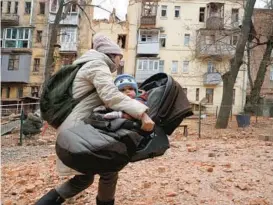  ?? ANDRII MARIENKO/AP ?? A mother whisks her child to safety as they flee a residentia­l building hit by Russian shelling Monday in Kharkiv, Ukraine. The war will hit the one-year mark Feb. 24.