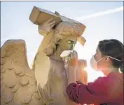  ??  ?? EVELYN ASKEW cleans an angel statue that was damaged and spray-painted with the word “Jehovah.”