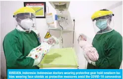  ??  ?? BIREUEN, Indonesia: Indonesian doctors wearing protective gear hold newborn babies wearing face shields as protective measures amid the COVID-19 coronaviru­s pandemic at a clinic in Bireuen, Aceh province. — AFP
