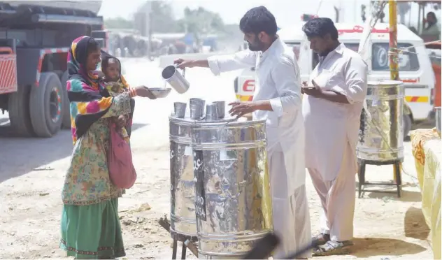  ?? Agence France-presse ?? ↑
Volunteers distribute water to a woman carrying a child along a street during a hot summer day in Karachi on Saturday.