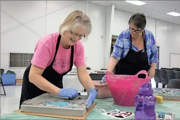  ?? Kristina Wilder / RN-T ?? Linda Munoz (left) and Jane Nuckles, both of Mentone, Alabama, grout the stepping stones to keep the designs in place.