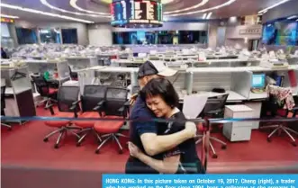  ?? — AFP ?? HONG KONG: In this picture taken on October 19, 2017, Cheng (right), a trader who has worked on the floor since 1994, hugs a colleague as she prepares to leave on her last day of work at the Hong Kong Stock Exchange.