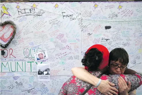  ?? LEAL-OLIVAS / AFP / GETTY IMAGES ?? Two women embrace Thursday in front of messages left on a wall of condolence following the deadly blaze at Grenfell Tower.