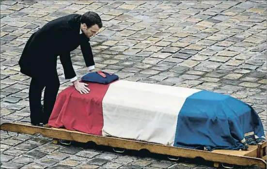  ?? PHILIPPE LOPEZ / AFP ?? El presidente francés, Emmanuel Macron, rinde tributo al gendarme muerto, sus manos sobre el féretro, en el patio de los Inválidos