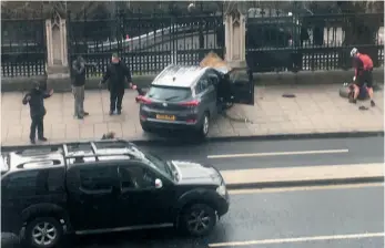  ?? AP PHOTO ?? People stand near a crashed car and an injured person lying on the ground, right, on Bridge Street near the Houses of Parliament in London on Wednesday.