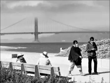  ?? AP Photo/Noah Berger ?? With the Golden Gate Bridge in the background, walkers wear masks while strolling at Crissy Field East Beach in San Francisco on Oct. 22.