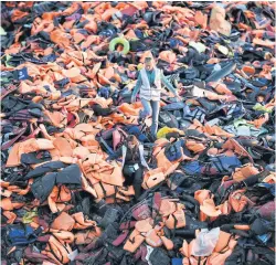  ?? AFP ?? Volunteers walk on a pile of life jackets left behind by refugees and migrants who arrived to the Greek island of Lesbos after crossing the Aegean sea from Turkey on Dec 3.