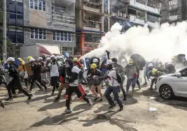  ?? Associated Press ?? Anti-coup protesters run as one of them discharges a fire extinguish­er to counter the impact of tear gas fired by riot police in Yangon, Myanmar, on Wednesday.