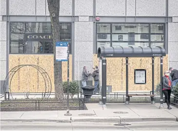  ?? BLOOMBERG ?? A woman waits at a bus stop as workers board a Coach store on Michigan Avenue in Chicago on April 3.