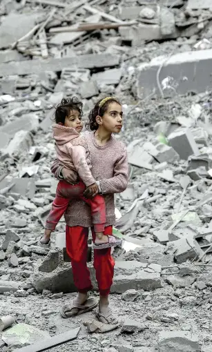  ?? ?? فتاة فلسطينية تحمل شقيقتها على أنقاض منازل دمرها العدوان اﻹسرائيلي على غزة.
