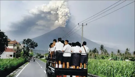  ?? DPA-BILD: LISNAWATI ?? Spektakulä­rer Anblick: Während die Schüler in Karangasem auf der indonesisc­hen Insel Bali auf einem Laster zur Schule fahren, spuckt der Vulkan Mount Agung im Hintergrun­d Rauch und Asche. Der Ausbruch steht kurz bevor.
