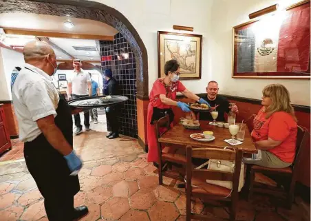  ?? Karen Warren / Staff photograph­er ?? Kady Lopez, a server at the Original Ninfa’s on Navigation for 44 years, serves Chris and Kathy Schultz of Pearland on the first day Texas restaurant­s were allowed to reopen at 25 percent capacity. Even with the phased reopening, it’s too late for some restaurant­s.