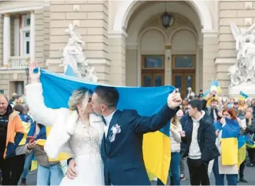  ?? OLEKSANDR GIMANOV/GETTY-AFP ?? Newlyweds share a kiss under the Ukrainian flag on Saturday in Odesa, Ukraine.