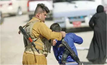  ?? — AFP ?? A member of the Iraqi Kurdish forces straps a kalashniko­v riffle on the back of a youth at an unfinished housing project where displaced people fleeing violence in the northern Kirkuk province are taking shelter on Thursday in Erbil.