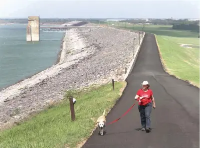  ?? Jerry Larson photos/Waco Tribune-Herald via AP ?? above
Naomi DiRago walks her dog, Luna, March 25 on the newly repaved Lake Waco Dam Trail in Waco, Texas. The trail has reopened after nearly six months of closures for the sake of a $1
million project to reinforce the dam. Meanwhile, two seasonal...