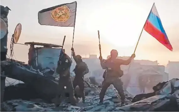  ?? Picture: AFP ?? Members of Wagner group wave a Russian national flag and Wagner Group's flag on the rooftop of a damaged building in Bakhmut.