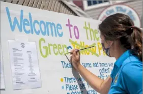  ??  ?? Server Amanda Sivillo paints a green phase sign outside of The Sloppy Duck Saloon in Erie.