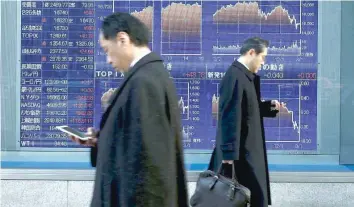  ?? — Reuters ?? Men walk past an electronic board showing market indices outside a brokerage in Tokyo.