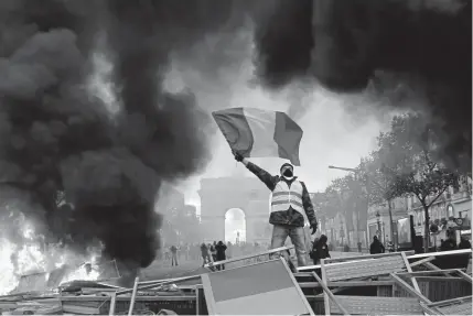  ?? Michel Euler, The Associated Press ?? During a protest of fuel taxes, a demonstrat­or stands on a burning barricade on the Champs-elysees, with the Arc de Triomphe in the background, on Saturday in Paris.